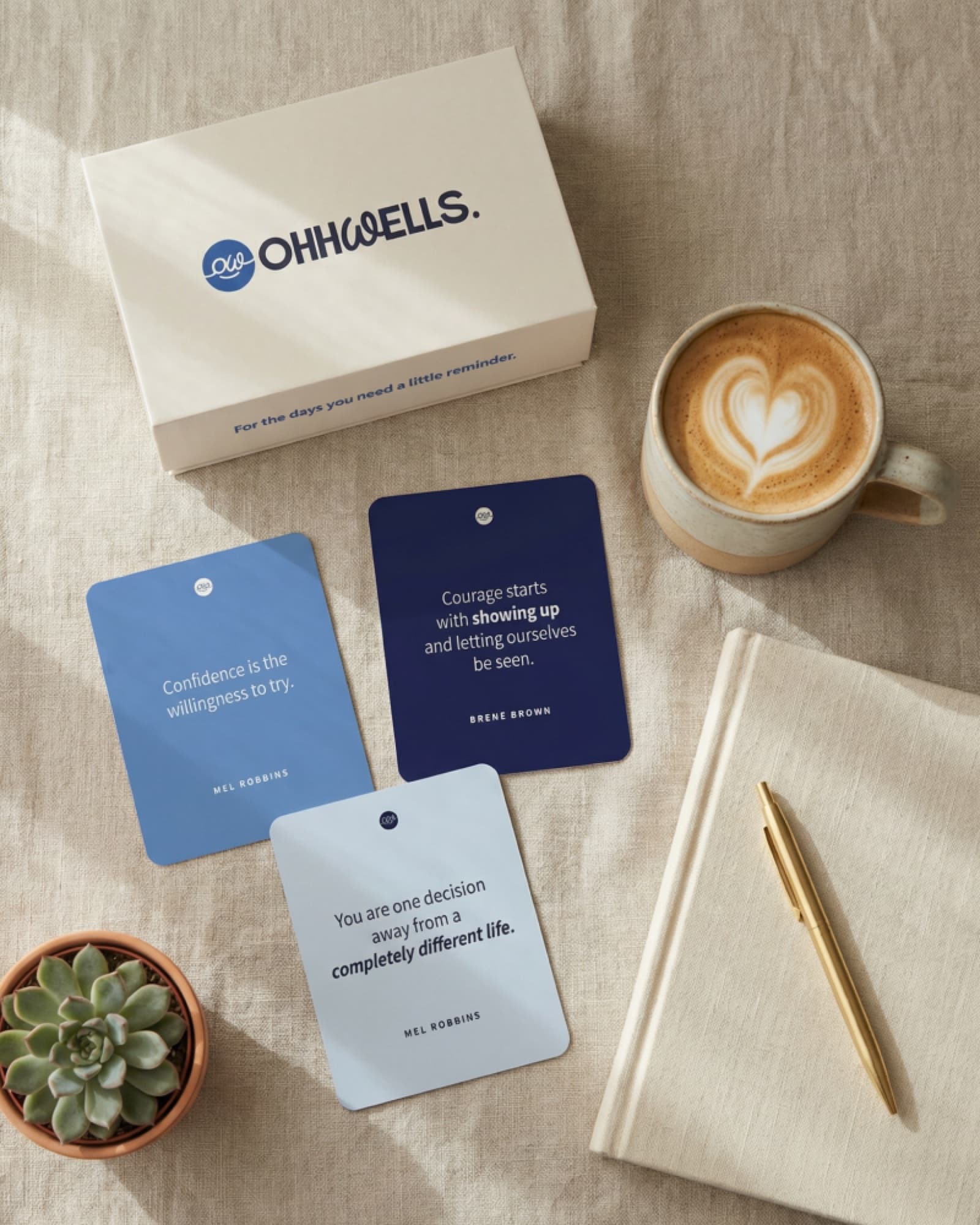 Flat lay of OhhWells kit with affirmation cards, coffee, and notebook